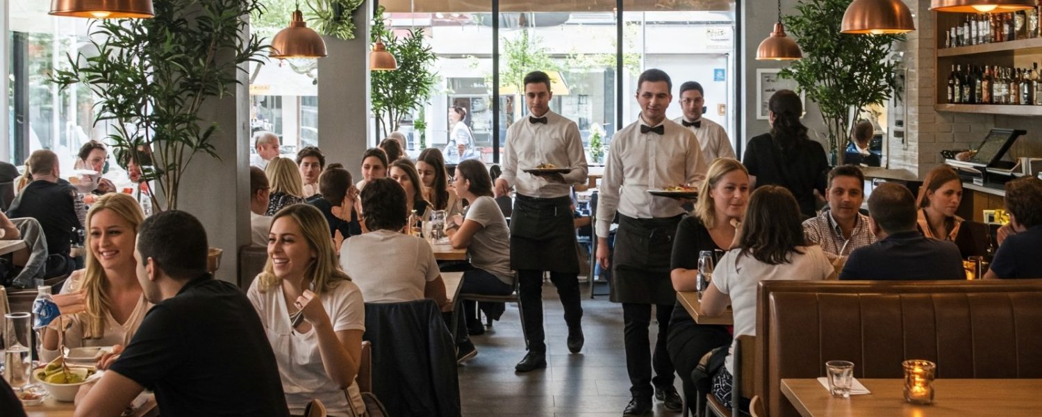 Customers dining inside a modern restaurant with staff serving food in a busy dining area